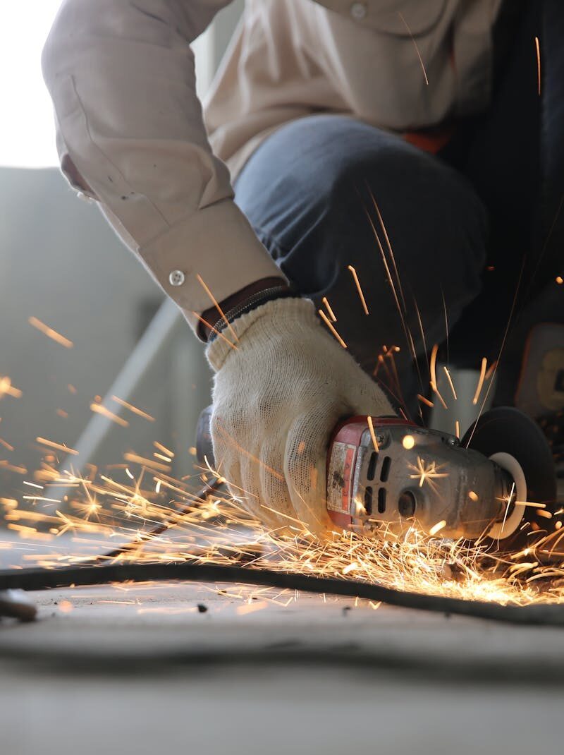 A skilled industrial worker uses a grinder creating a burst of sparks indoors.